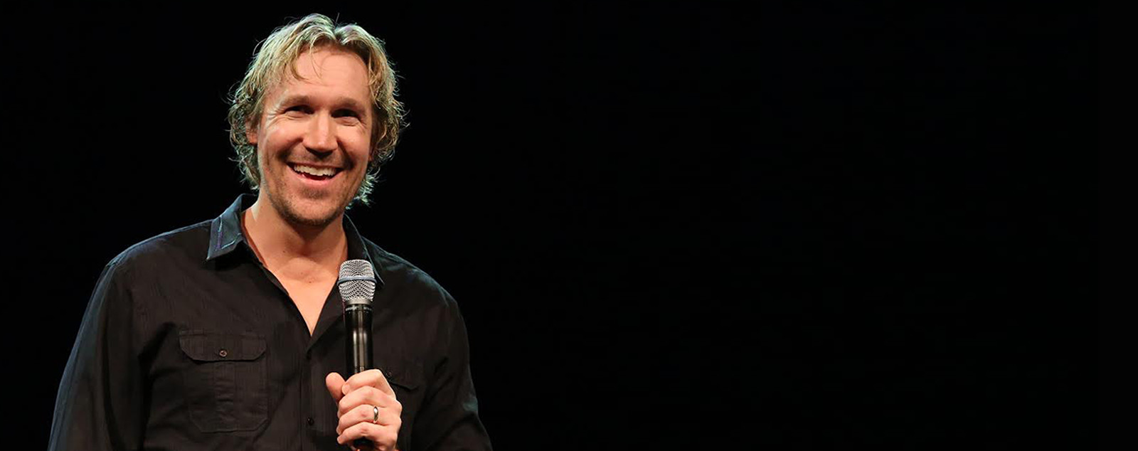 David A.R. White smiling on stage with a microphone